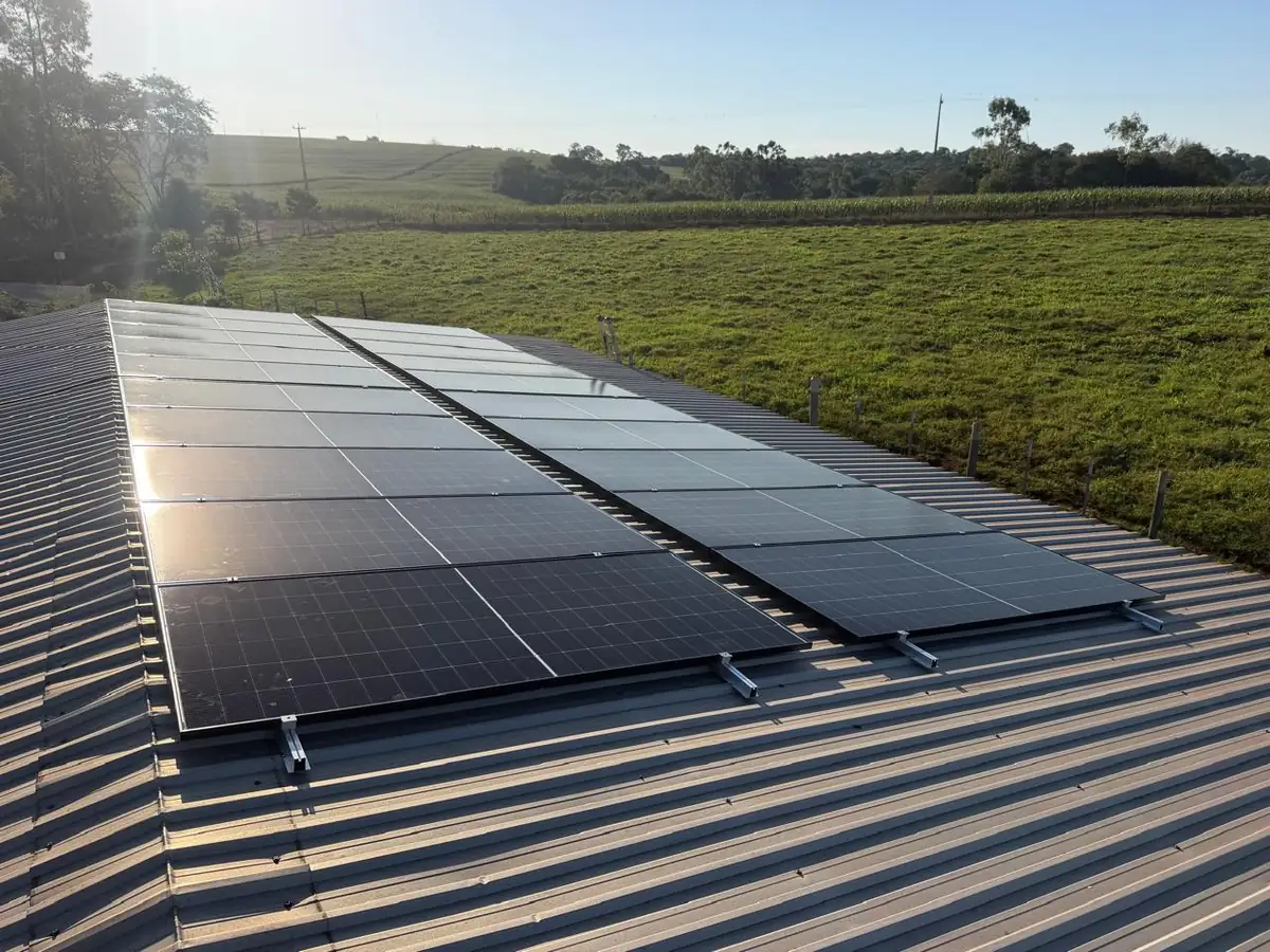 Placas solares em telhado metalico com lavoura ao fundo, zona rural de Mercedes